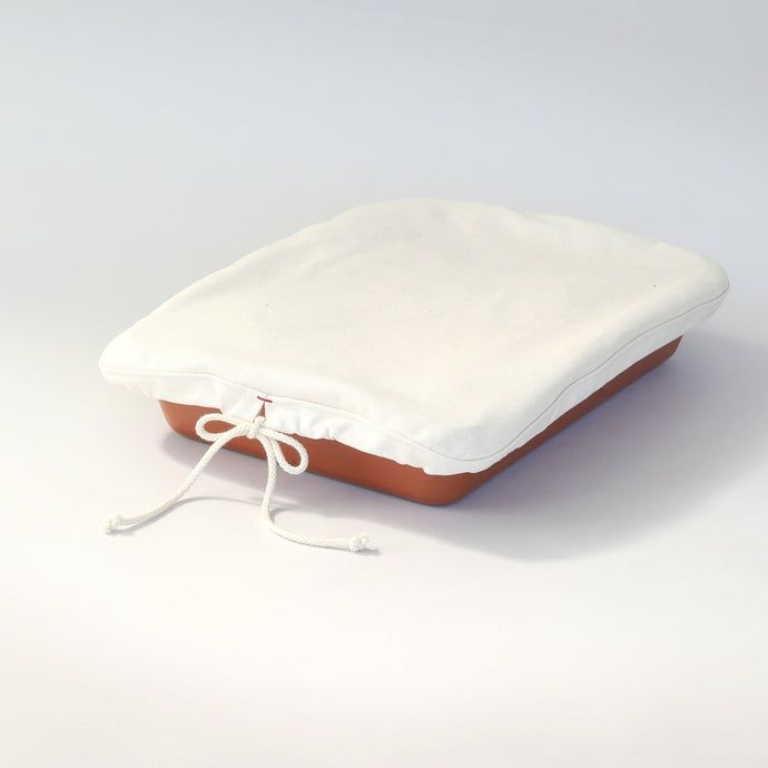 Natural colored cloth with a tied drawstring fitted over a red rectangular serving dish.