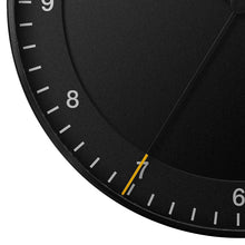 Load image into Gallery viewer, Front detail view of round black clock on white background. The clock face is black and has a black seconds hand with a yellow tip. The hours are shown as white numbers.
