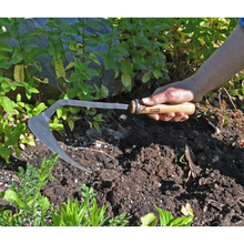Load image into Gallery viewer, Side view of a hook shaped metal hoe being held by a hand above loose dirt. 
