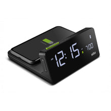 Load image into Gallery viewer, 3/4 view of black digital clock against a white background. The charging dock is attached behind the clock. A smartphone is charging on the dock. The clock face is black and can be illuminated.
