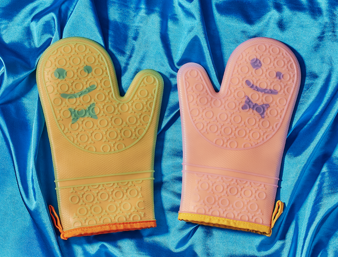 Image of two oven mitts on a shiny blue fabric background, yellow mitt on the left with a green smiley face and bowtie, pink mitt on the right with a purple smiley face and bow tie.