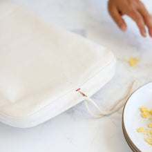 Load image into Gallery viewer, Close up of a marble counter top with the rectangular cloth cover and a stack of white plates holding yellow cake crumbs.
