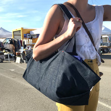 Load image into Gallery viewer, Outdoor scene of a market in a parking lot. In the foreground a woman dressed in yellow trousers and a white crochet top holds a large denim tote on her shoulder.
