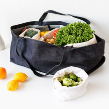 Load image into Gallery viewer, Large denim tote placed on a white top. Inside the tote are numerous cloth bags filled with colorful produce.
