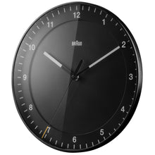 Load image into Gallery viewer, Left 3/4 view of round black clock on white background. The clock face is black and has black hour and minute hands with white tips. The seconds hand is black with a yellow tip. The hours are shown as white numbers.
