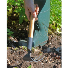 Load image into Gallery viewer, Image of a person in a garden holding a 3 tine garden cultivator rake over loose dirt.
