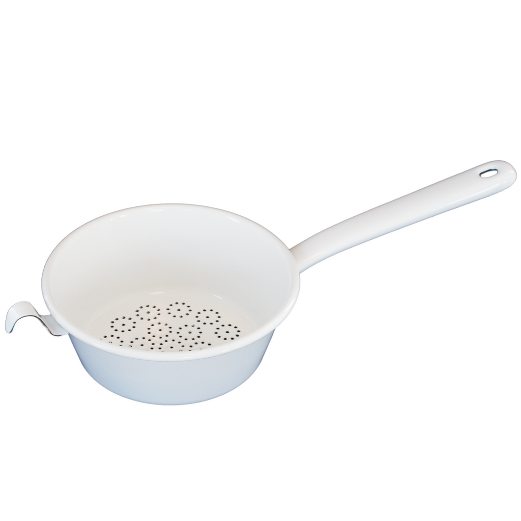 A top down angled view into a small pan with a floral perforation on the bottom, the left hand side has a small hook attached to the lip opposite to the handle that protrudes to the right.